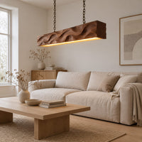 Long wood pendant light with carved waves and a warm glow along its underside in a Scandinavian living room with white walls