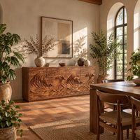 Sideboard with four doors carved in a rolling ocean wave relief in a bright dining room with arched windows and plants