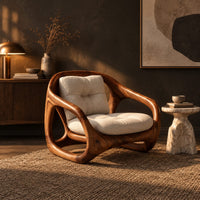 Chair with a sculpted open loop wood frame and tufted cream cushions in a dark living room at golden hour