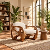 Chair with a chunky sculpted frame, large oval cutouts and a pillow back in a bright living room with arched windows and plants