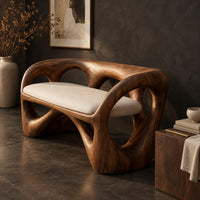 Corner detail of bench with a looped wooden frame, cutout back and cream cushion beside wood, brass and linen samples
