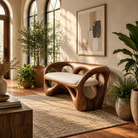 Bench with a looped wooden frame, cutout back and cream cushion in a bright entryway with arched windows and plants