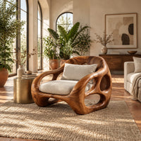 Chunky lounge chair with circular cutouts in thick sculpted arms in a bright living room with arched windows and plants