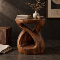 Corner detail of chunky side table with a looping open body and thick flat top beside wood, brass and linen samples