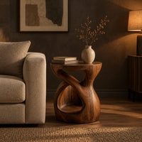 Chunky side table with a looping open body and thick flat top in a dark living room at golden hour