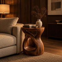 Chunky side table with a looping open body and thick flat top in an evening living room with walnut wall paneling