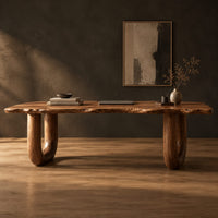 Desk with a live edge slab top and two thick sculpted legs in a dark studio against a charcoal plaster wall