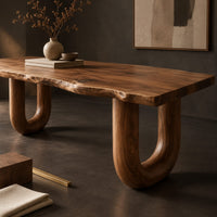 Corner detail of desk with a live edge slab top and two thick sculpted legs beside wood, brass and linen samples