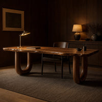 Desk with a live edge slab top and two thick sculpted legs in an evening home office with walnut wall paneling