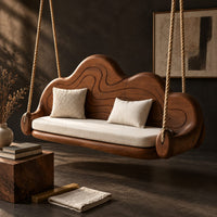 Corner detail of cloud shaped swing with a carved wavy backrest and cream seat cushion beside wood, brass and linen samples