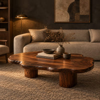 Low coffee table with a cloud shaped wavy top on thick cylinder legs in a dark living room at golden hour