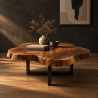 Cloud shaped coffee table with a thick slab top on a slim cross base in a dark studio against a charcoal plaster wall
