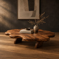 Cloud shaped coffee table with a thick wavy top and angled legs in a dark studio against a charcoal plaster wall