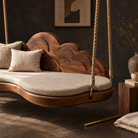Corner detail of cloud shaped swing with a scalloped carved back and a padded seat beside wood, brass and linen samples