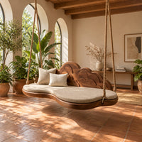 Cloud shaped swing with a scalloped carved back and a padded seat in a bright porch with arched windows and plants