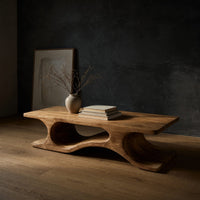 Minimal coffee table with an S curve waist base in a dark studio against a charcoal wall