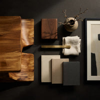 Corner detail of minimal coffee table with an S curve waist base beside wood, brass and linen samples