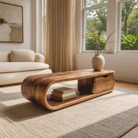 Long loop coffee table with a side drawer box in a sunlit room with large windows and plants