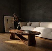 Coffee table on angled plank legs with a swooping brace in a dark studio against a charcoal wall