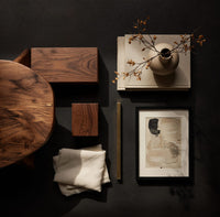 Corner detail of coffee table on angled plank legs with a swooping brace beside wood, brass and linen samples