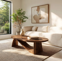 Coffee table on angled plank legs with a swooping brace in a sunlit room with large windows and plants