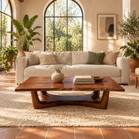Rectangular coffee table on an arched trestle base with a low curved beam in a bright living room with arched windows and plants