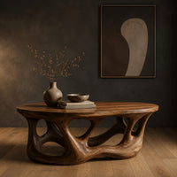 Oval coffee table with a branching root shaped base full of irregular openings in a dark studio against a charcoal plaster wall
