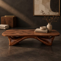 Corner detail of low coffee table with a carved organic base and a soft edged top beside wood, brass and linen samples