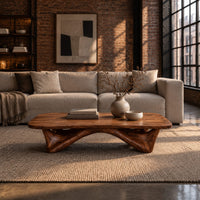 Low coffee table with a carved organic base and a soft edged top in an industrial loft living room with exposed brick
