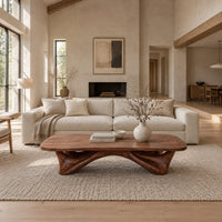 Low coffee table with a carved organic base and a soft edged top in a bright open plan living room