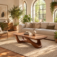 Coffee table with an irregular soft edged top on sculpted branching legs in a bright living room with arched windows and plants