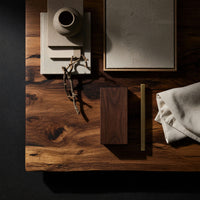 Corner detail of coffee table with rolled ends and a double open shelf beside wood, brass and linen samples
