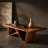 Corner detail of coffee table with a tapered block pedestal and a swooping wood loop beside wood, brass and linen samples