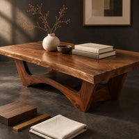 Corner detail of coffee table with a thick slab top and arched pedestal legs beside wood, brass and linen samples