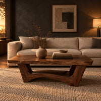 Coffee table with a thick slab top and arched pedestal legs in a dark living room at golden hour