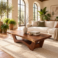 Coffee table with a thick slab top and arched pedestal legs in a bright living room with arched windows and plants