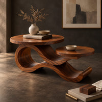 Corner detail of wooden coffee table with two circular tops on a swooping ribbon base beside wood, brass and linen samples