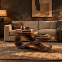 Wooden coffee table with two circular tops on a swooping ribbon base in a dark living room at golden hour