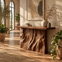 Console table with a deeply ridged sculpted block base in a bright entryway with arched windows and plants