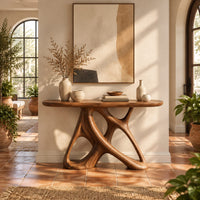 Oval console table on an open base of twisting interlocked loops in a bright entryway with arched windows and plants