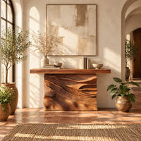 Console table with a solid block base carved in dune ripples in a bright entryway with arched windows and plants
