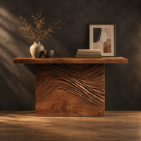 Console table with a thick plank top and wave carved block base in a dark studio against a charcoal plaster wall
