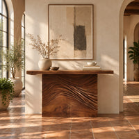Console table with a thick plank top and wave carved block base in a bright entryway with arched windows and plants