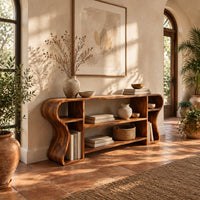 Open shelf console table with wavy curved ends and a divided center bay in a bright entryway with arched windows and plants
