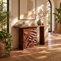 Console table with plank legs and a dune carved panel in a bright entryway with arched windows and plants