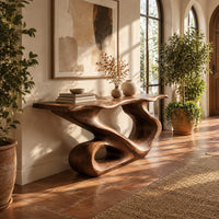Narrow console table with a flowing s shaped base and an open loop foot in a bright entryway with arched windows and plants