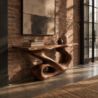 Narrow console table with a flowing s shaped base and an open loop foot in an industrial loft entryway with exposed brick