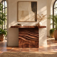 Console table with a thick top on a wave carved block base in a bright entryway with arched windows and plants