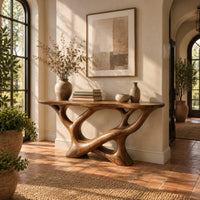 Oval top console table on a sculpted base of looping open limbs in a bright entryway with arched windows and plants