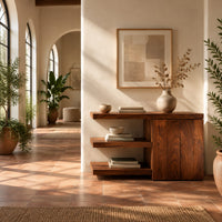 Console table with open shelves and a two door cabinet in a bright entryway with arched windows and plants